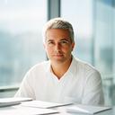 Professional portrait of a company founder in a glass-walled office with soft daylight and paperwork on the table